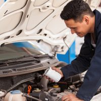 Young,Hispanic,Mechanic,Changing,The,Oil,Filter,Of,A,Car Young Hispanic mechanic changing the oil filter of a car at an auto shop